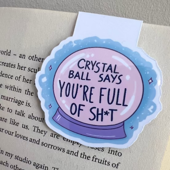 Sticker with 'Crystal Ball says you're full of sh*t' text on a book page