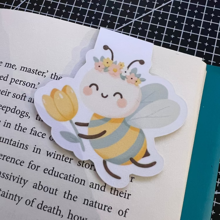 Bookmark shaped like a bee holding a tulip on a book page.