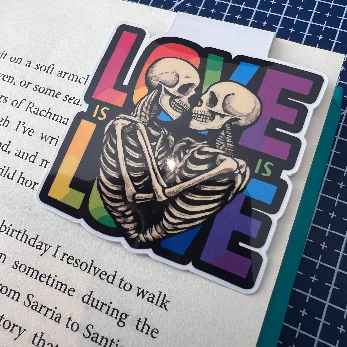 Sticker with skeletons embracing and 'LOVE IS LOVE' text on a book page.