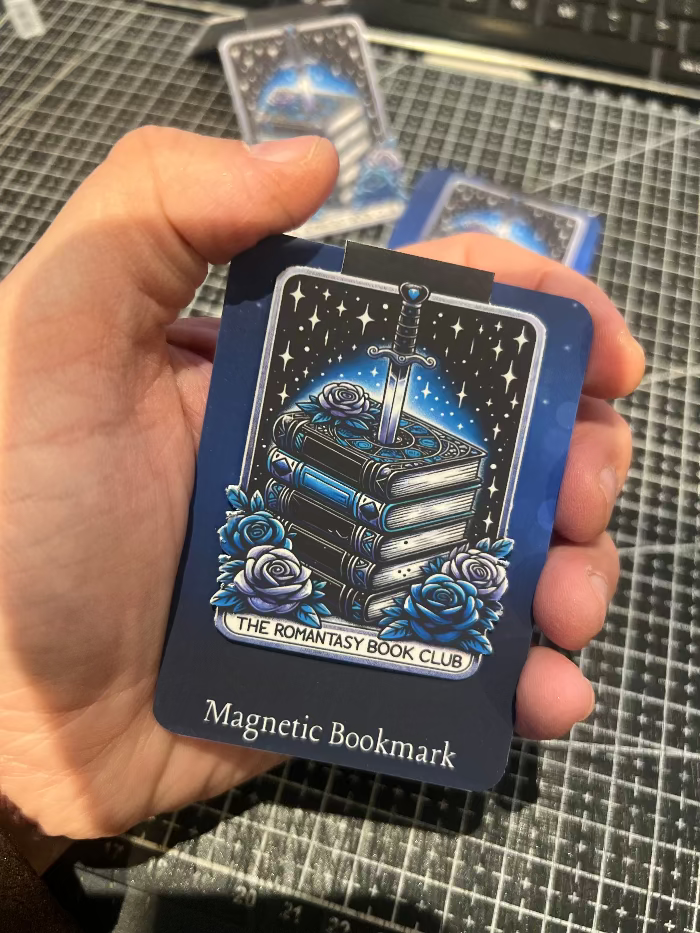 Magnetic bookmark with blue design and text held by a hand on a grid background