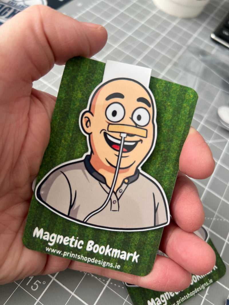 Hand holding a green magnetic bookmark with a cartoon character on a grid background