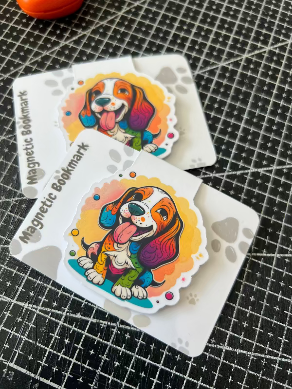 Two colorful dog-themed magnetic bookmarks on a black grid surface.