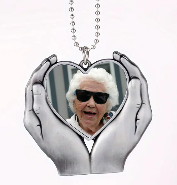 Heart-shaped pendant with hands holding a photo of an elderly woman wearing sunglasses on a white background