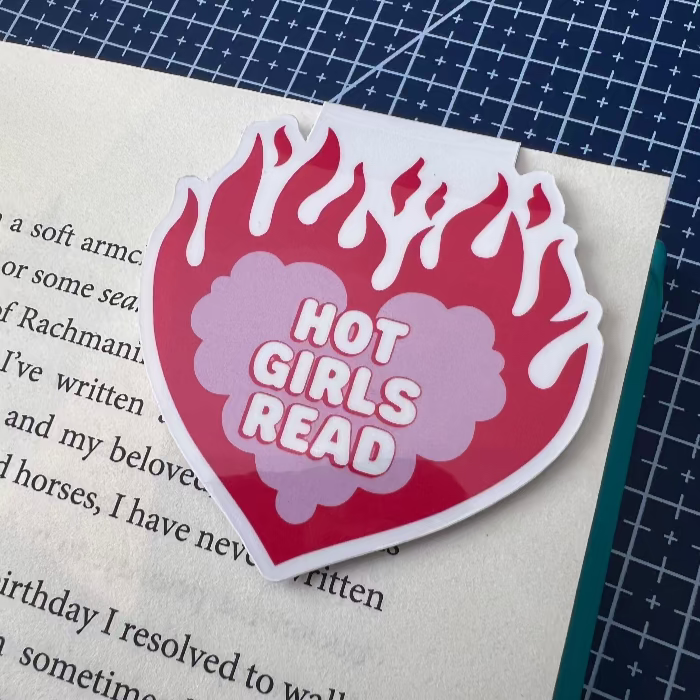 Heart-shaped 'Hot Girls Read' sticker on a book with a blue grid background