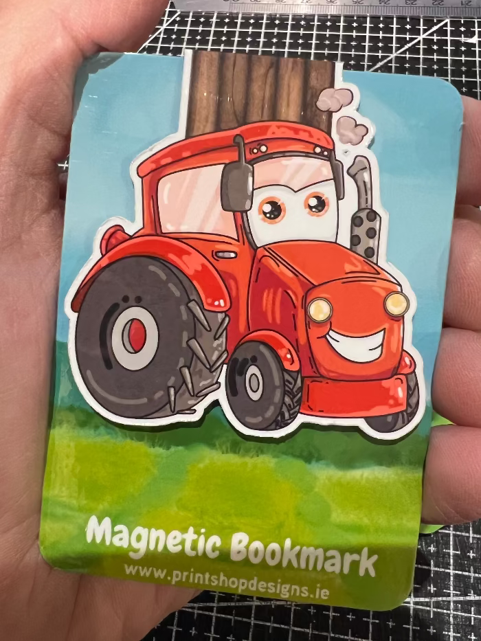 Magnetic bookmark with a cartoon red tractor design held by a hand.