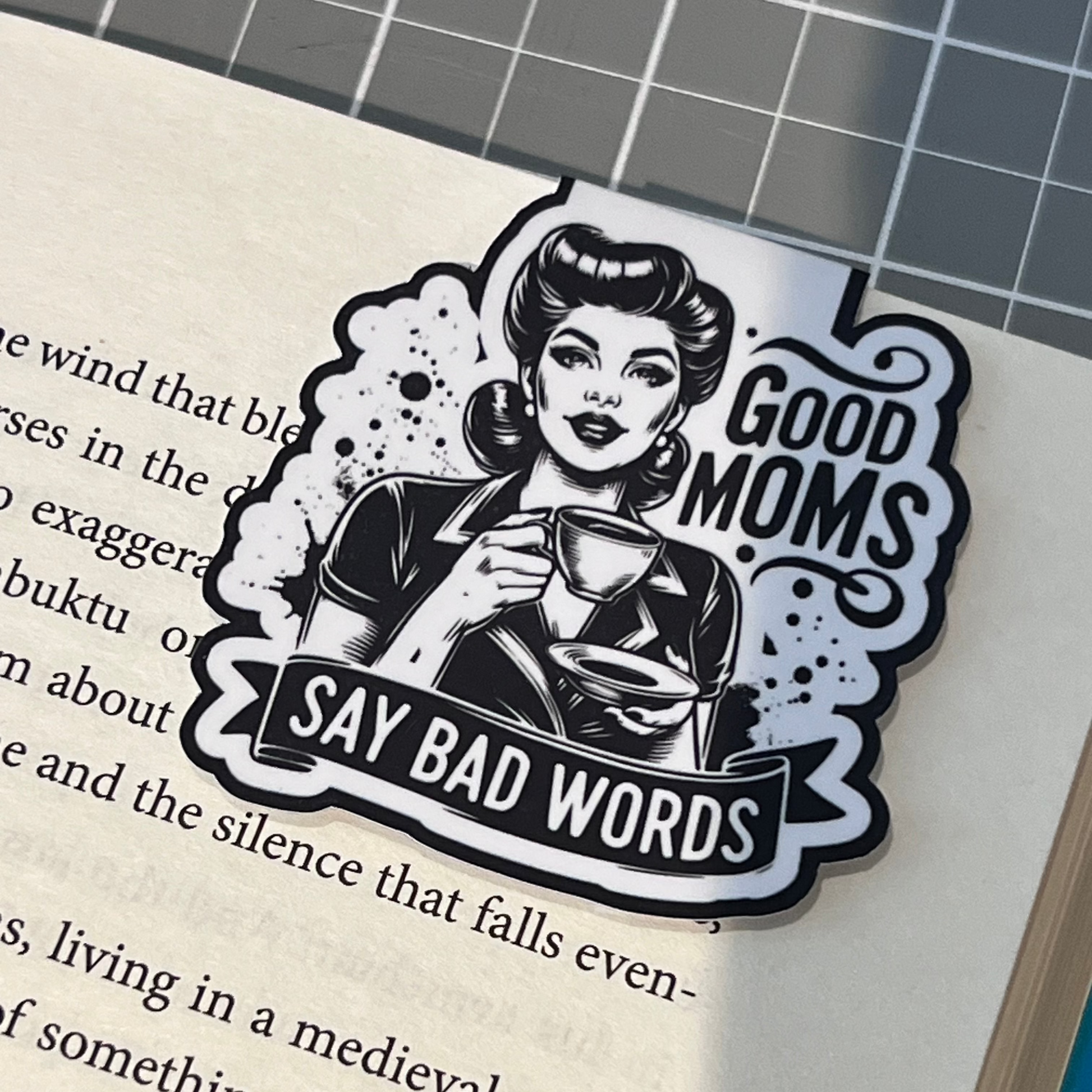 Sticker with graphic design of a woman and text 'Good moms say bad words' on a book page.