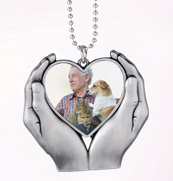 Heart-shaped pendant with a photo of a man with a dog and cat, held in two hands.