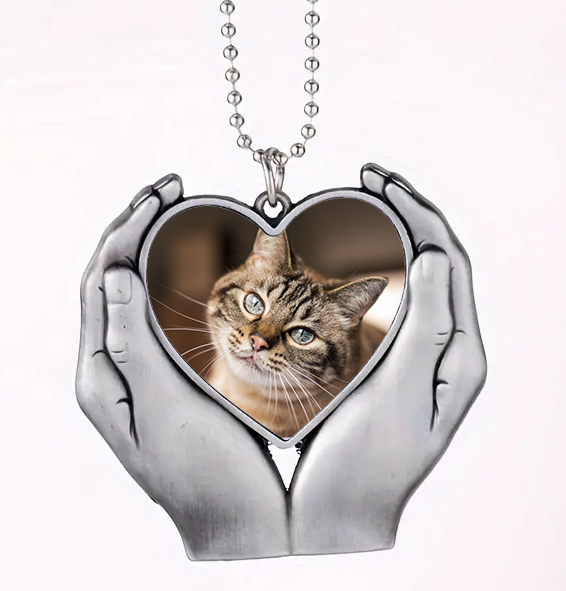 Heart-shaped pendant with a cat's face inside, held by two hands on a white background