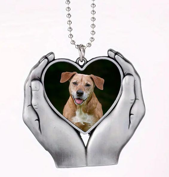 Heart-shaped pendant with a dog's photo held by two hands on a white background