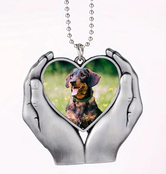 Heart-shaped pendant with a dog's photo held in hands on a white background