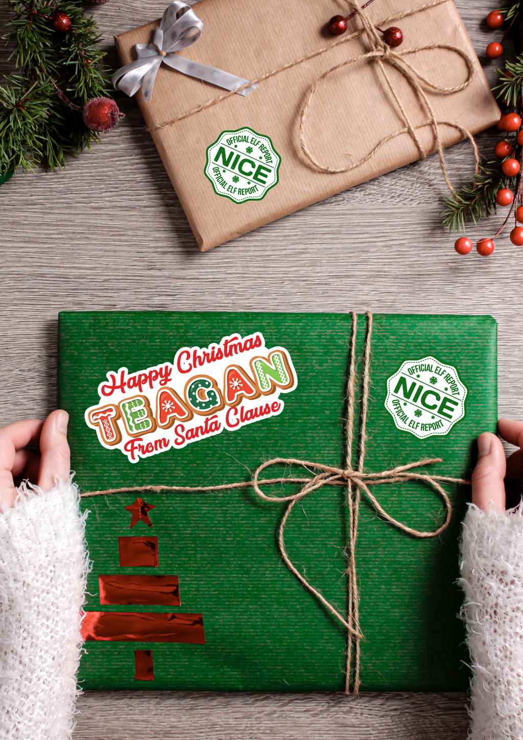 Green gift box with 'Happy Christmas Teagan from Santa Clause' text, tied with twine, on a wooden surface with a wrapped brown gift and Christmas decorations.
