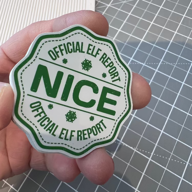 Hand holding a 'Nice' Official Elf Report sticker against a grid background