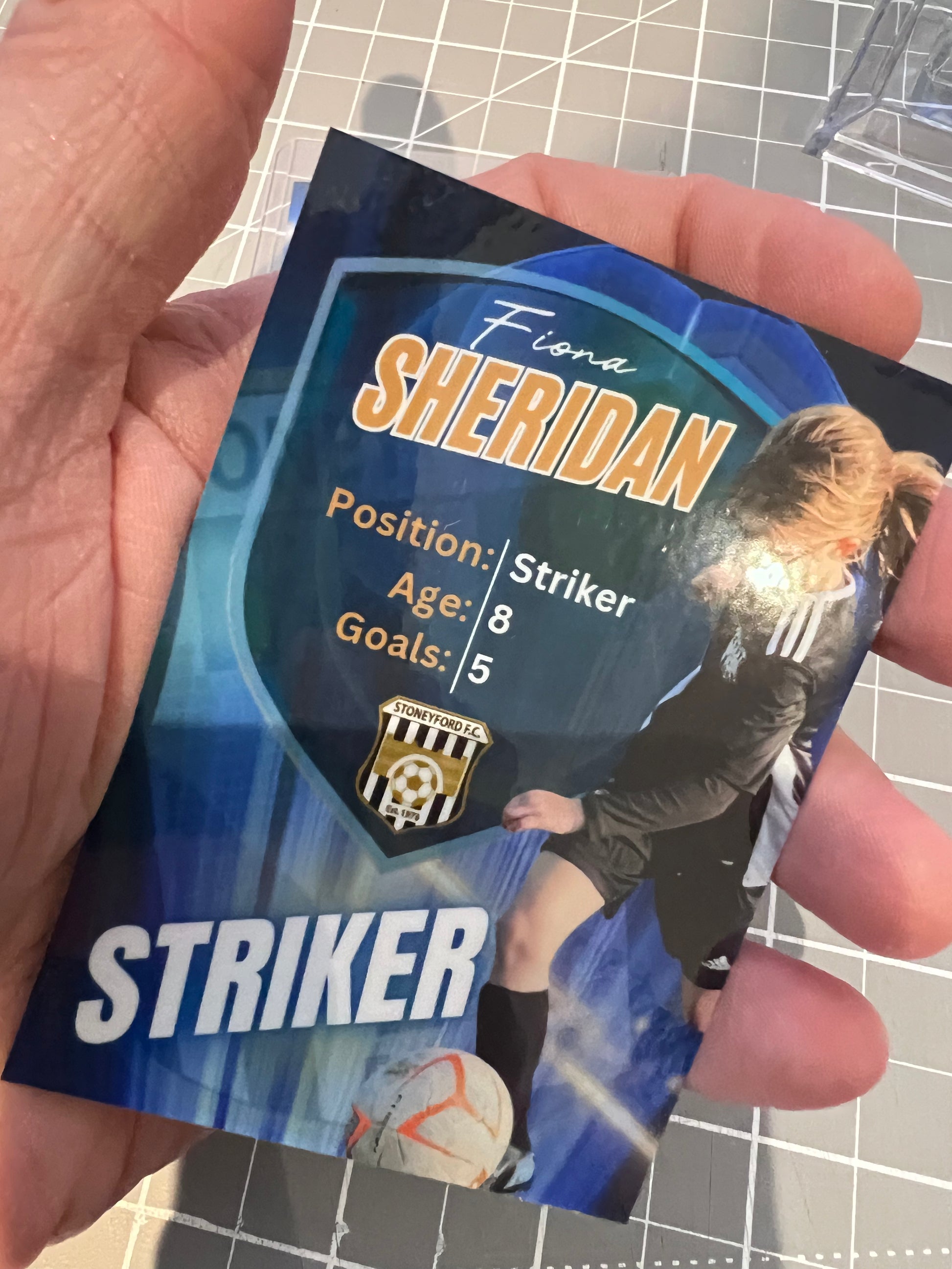 Hand holding a soccer trading card of Fiona Sheridan, a striker with the age 8 and 5 goals.