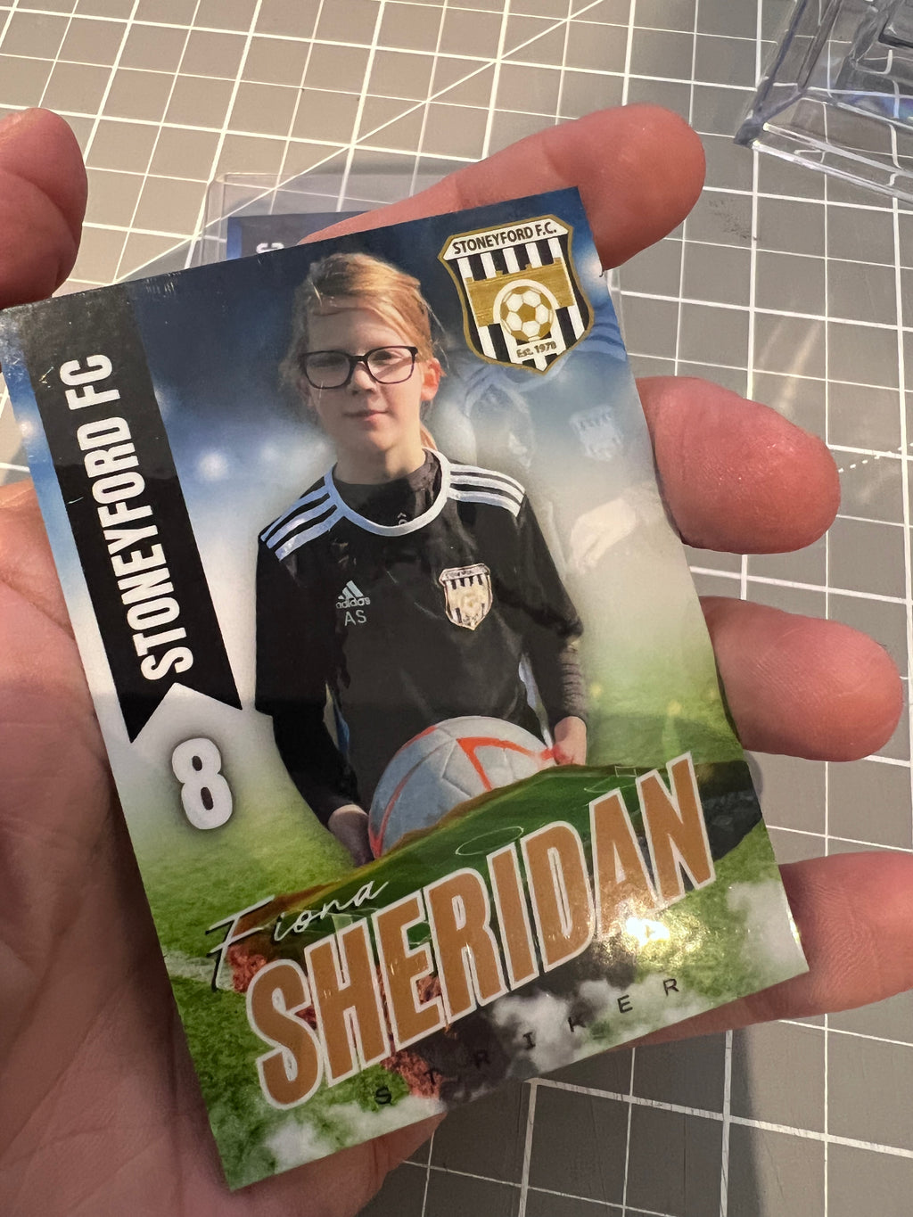 Card featuring a young boy with glasses holding a soccer ball, branded 'Stoneyford FC'.