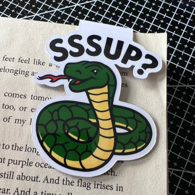 Sticker of a snake with 'SSSUP?' text on a book page