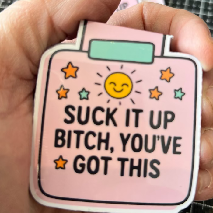 Pink bottle-shaped sticker with motivational text held in a hand