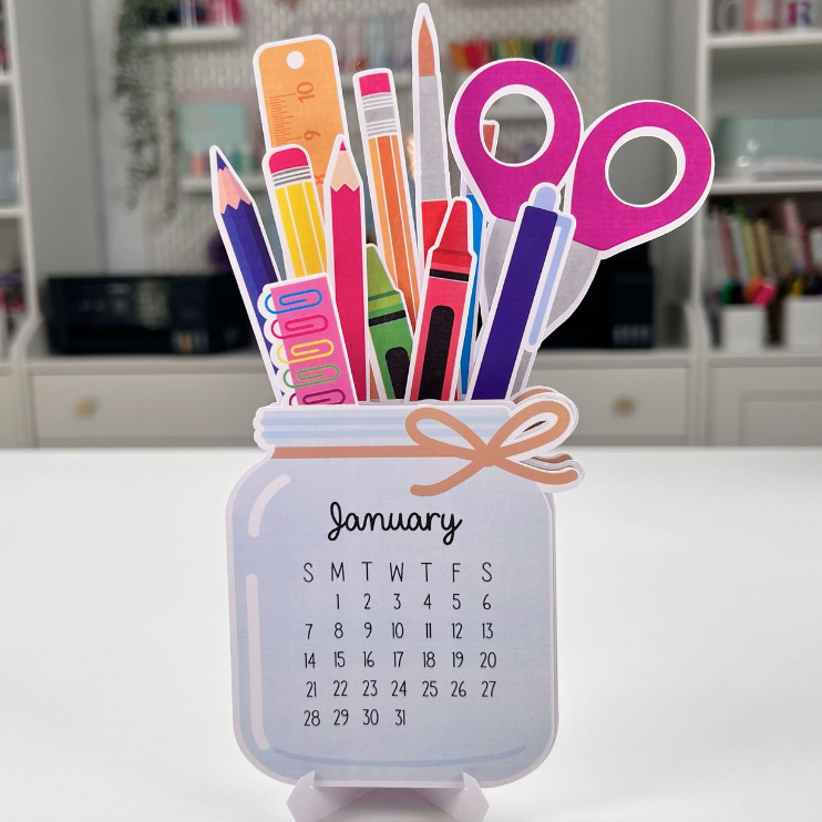 Calendar with stationery items on a stand in front of a bookshelf