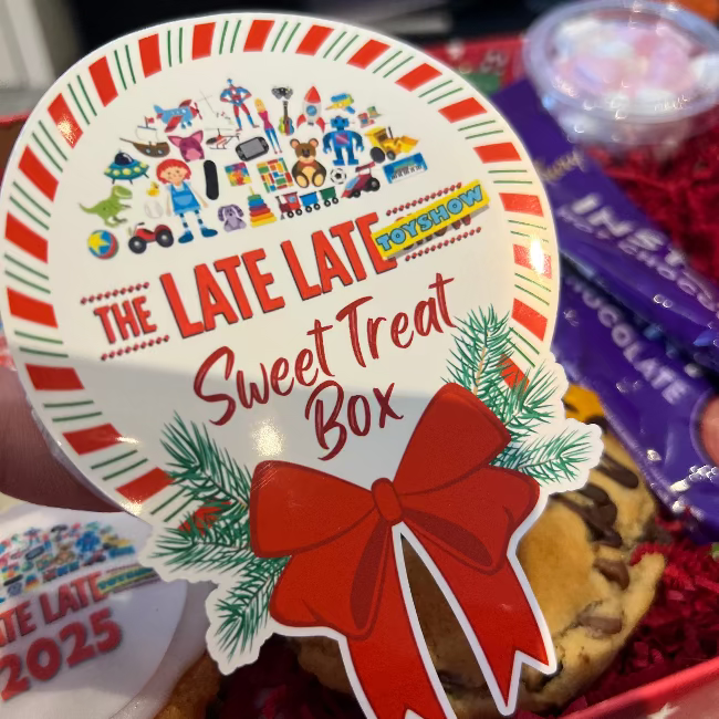 Decorative lid of a 'The Late Late Sweet Treat Box' with festive design and cookies underneath.